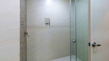 A modern bathroom with a glass shower enclosure, a tiled floor, and a wall-mounted light fixture.
