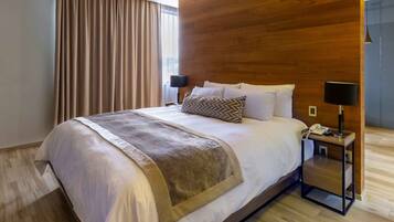 Habitació d'hotel moderna amb un llit gran, un panell de fusta al capçal i una tauleta de nit amb una làmpada.