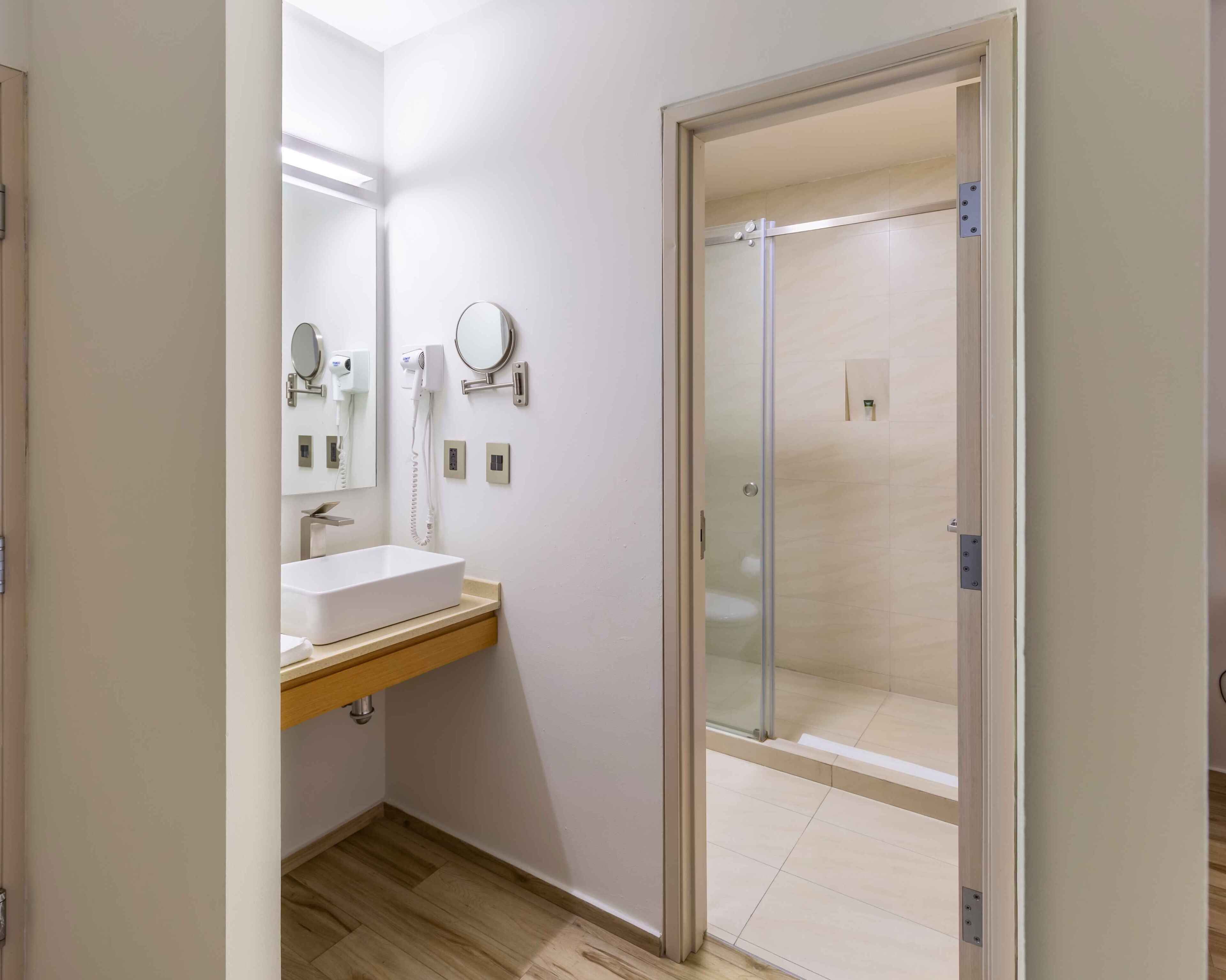 Un baño moderno con un lavamanos blanco, un espejo y una ducha con cerramiento de vidrio.