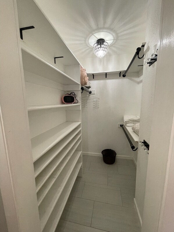 A narrow walk-in closet with white shelves, a hanging rack, and a ceiling light fixture. - Chic Large Austin Home For Families & Groups - sleeps 9+ Game Room and on 1 acre (Manchaca)