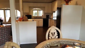 Een moderne keuken met witte kasten, een centraal eiland en een eetgedeelte met een tafel en stoelen.