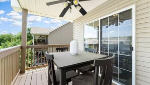 Un patio exterior techado con mesa y sillas, ventilador de techo y un ventanal grande.