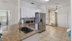 Uma cozinha moderna com bancadas de granito, eletrodomésticos de aço inoxidável e armários brancos.