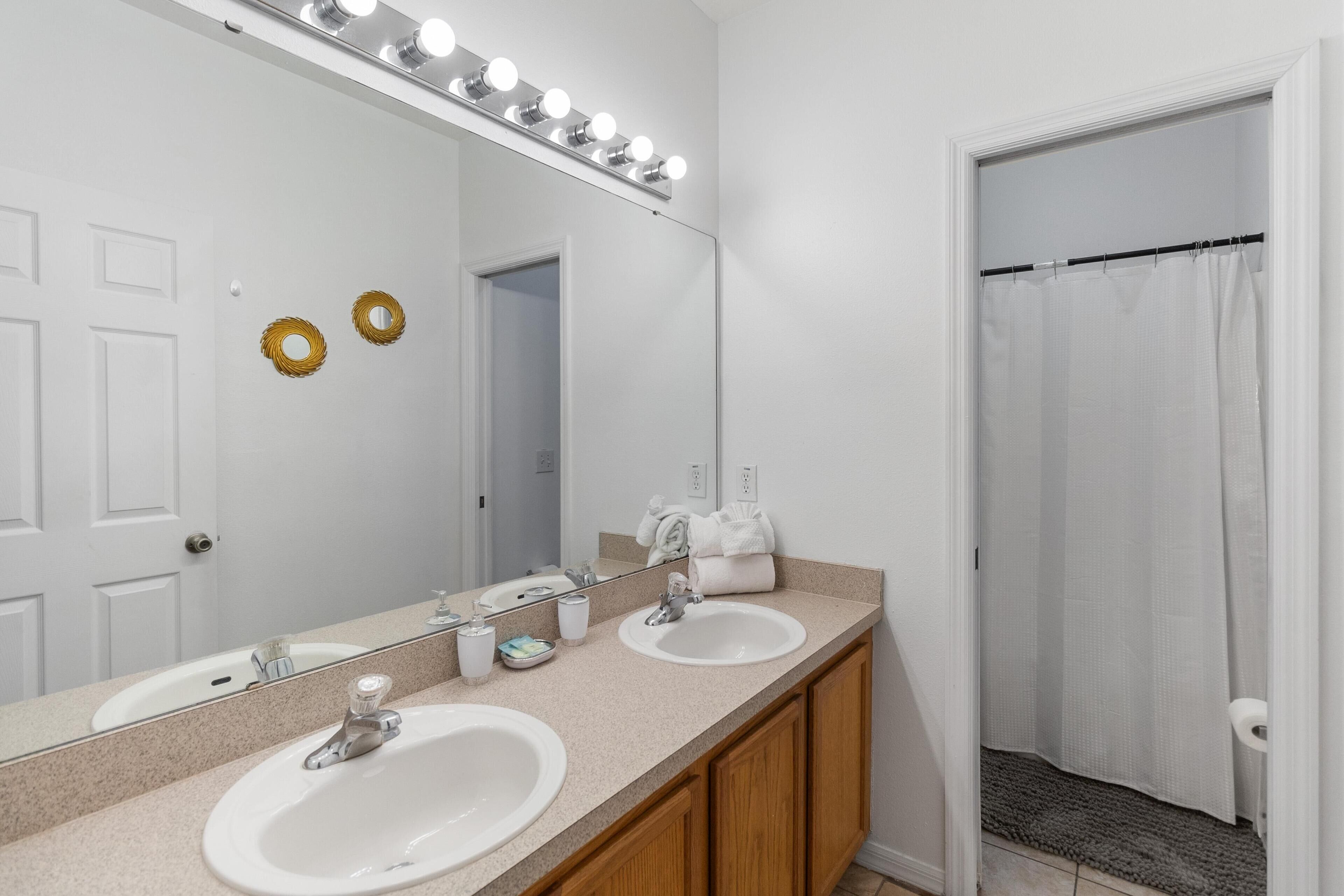 Un baño con dos lavamanos, un espejo grande iluminado y cortina de ducha.