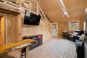 Et interiør med trævægge, et fjernsyn, en pejs, en sofa og en trappe.