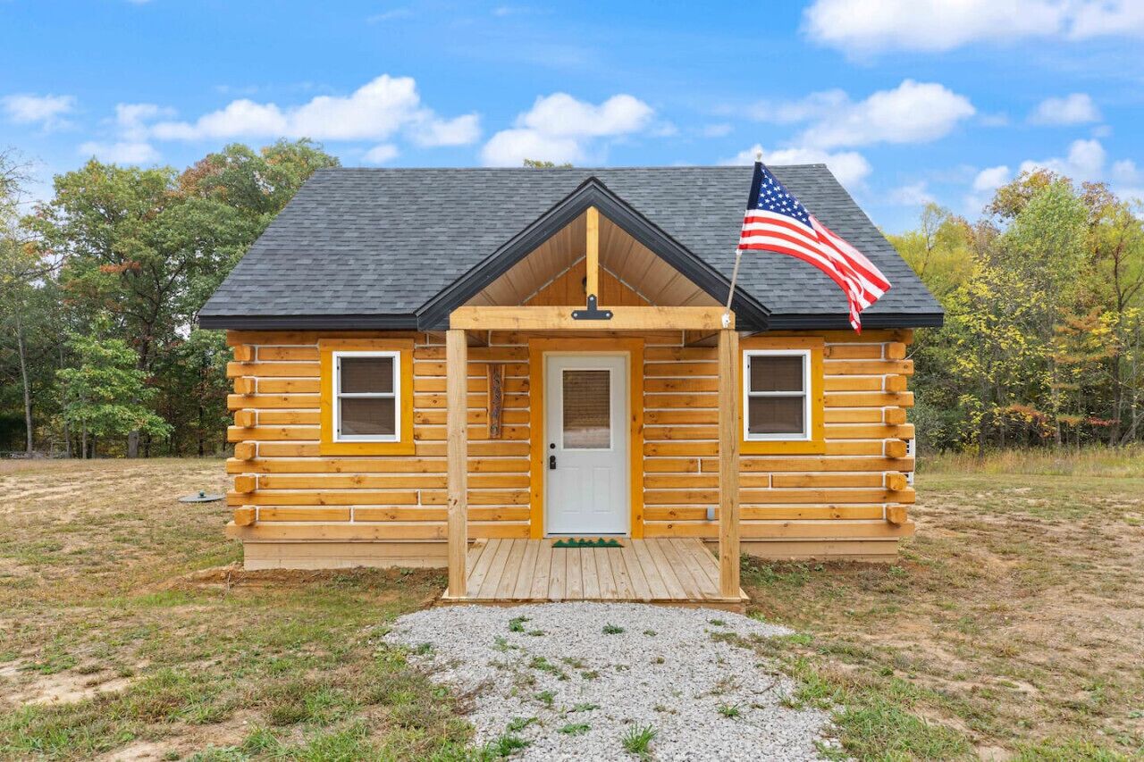 A log cabin with a front porch, a flag, and a door.