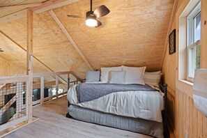 A cozy attic bedroom with a wooden ceiling, a bed with white bedding, and a window on the right.
