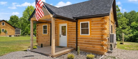 A wooden cabin with a porch, an American flag, and a small deck.