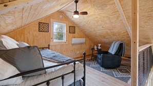 Ein gemütliches Schlafzimmer im Dachgeschoss mit Bett, Stuhl, Deckenventilator und Fenster.