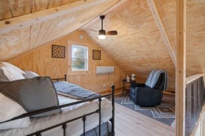 Une chambre mansardée accueillante, avec un lit, une chaise, un ventilateur de plafond et une fenêtre.