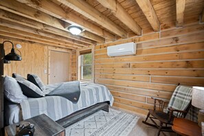 Et soveværelse i en træhytte med seng, stol, bord og en klimaanlæg.