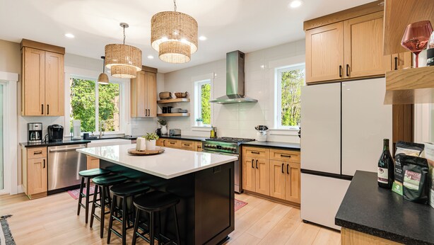 A modern kitchen with wooden cabinets, a large island with stools, stainless steel appliances, and pendant lighting. - Avery House in Newberg: 6 bedrooms, forest views, sleeps 12, ideal for family getaways (Newberg)
