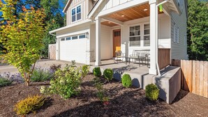 A two-story house with a covered porch, a garage, and a landscaped garden with various shrubs and a tree. - Avery House in Newberg: 6 bedrooms, forest views, sleeps 12, ideal for family getaways (Newberg)