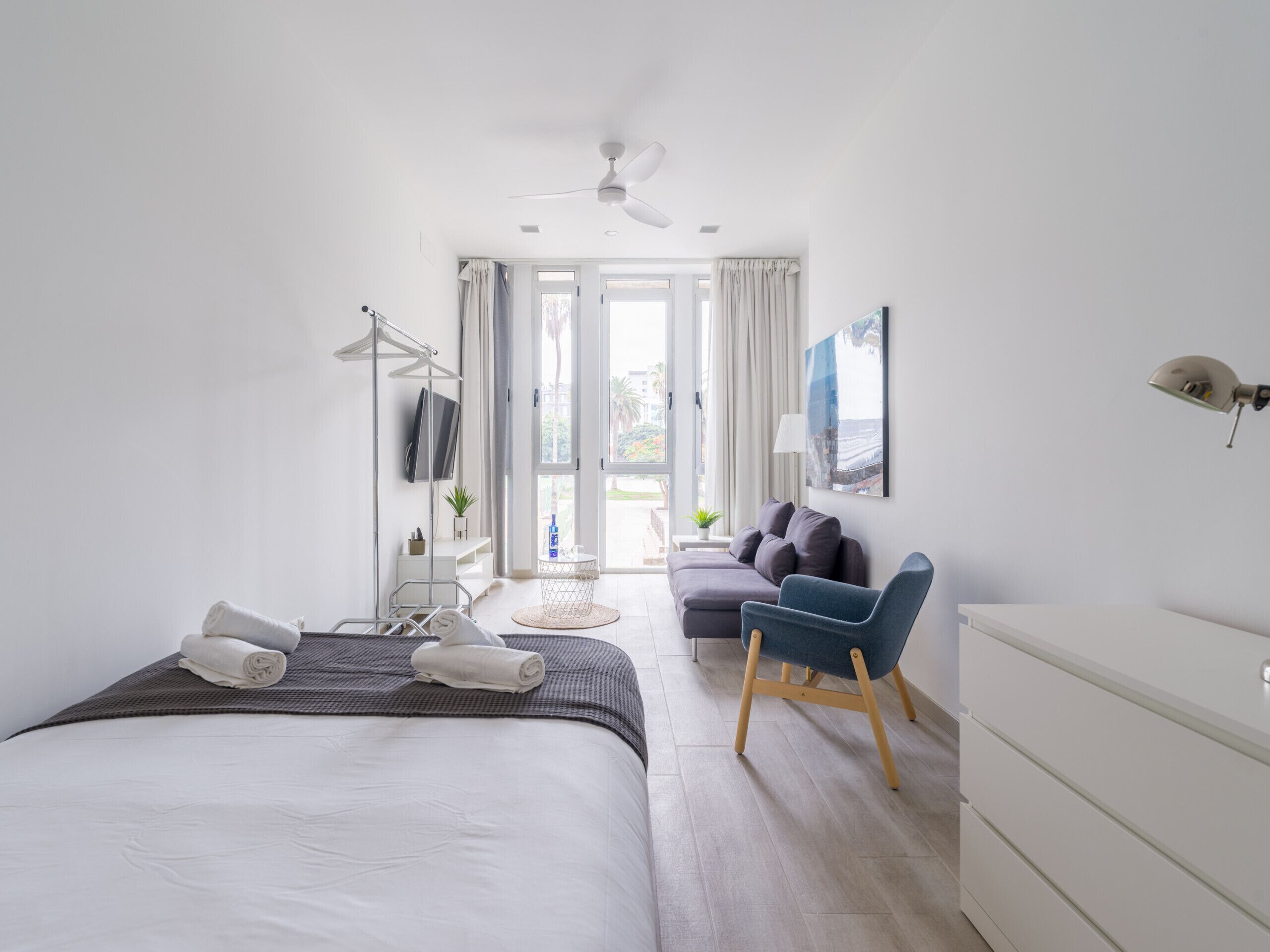 A modern bedroom with a bed, a desk, a chair, a TV, and a view of the outdoors.