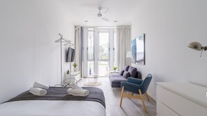 A modern bedroom with a bed, a desk, a chair, a TV, and a view of the outdoors.