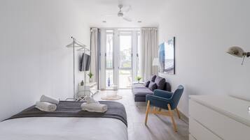 A modern bedroom with a bed, a desk, a chair, a TV, and a view of the outdoors.