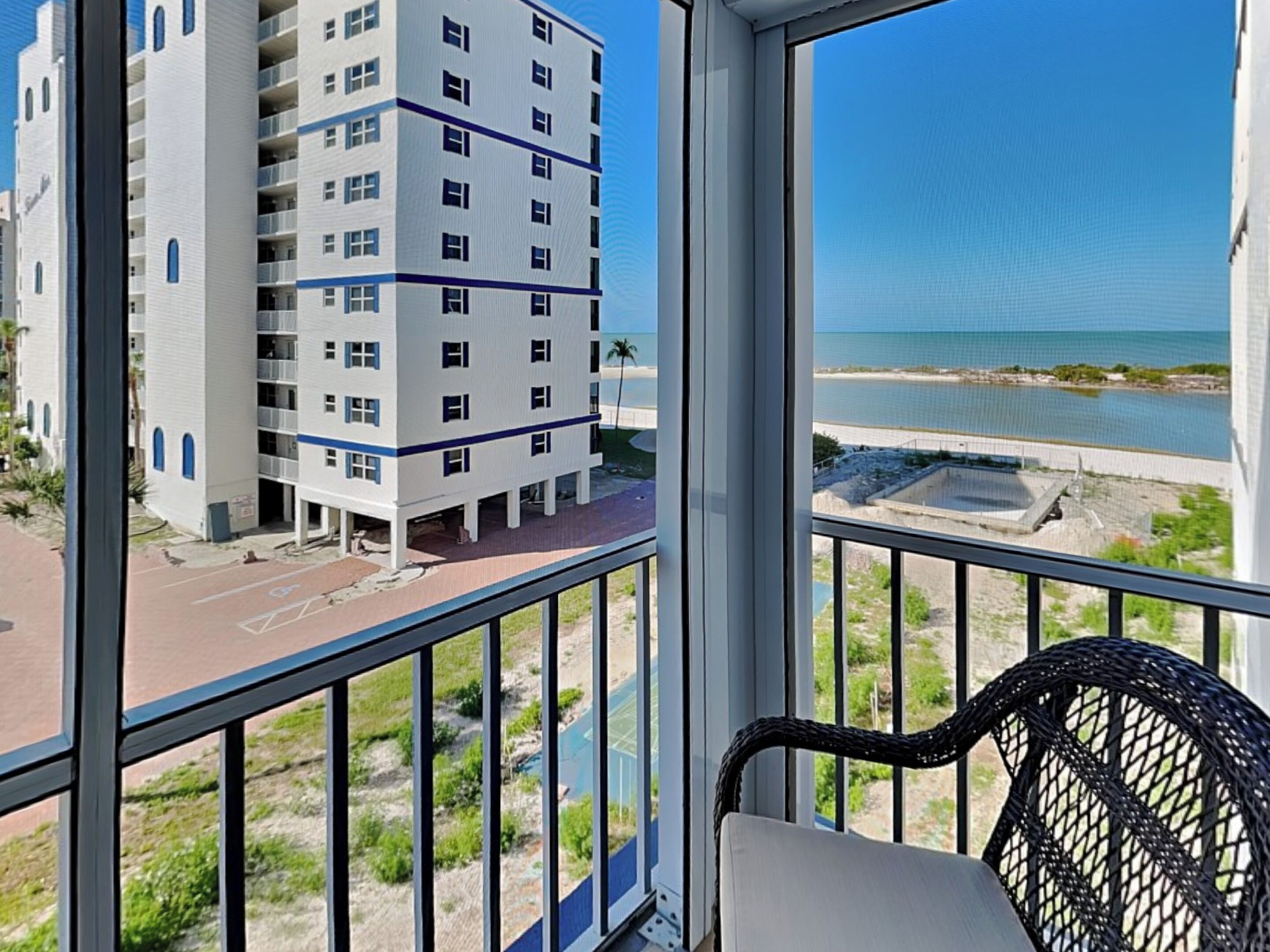A balcony with a view of a beachfront and a multi-story building.