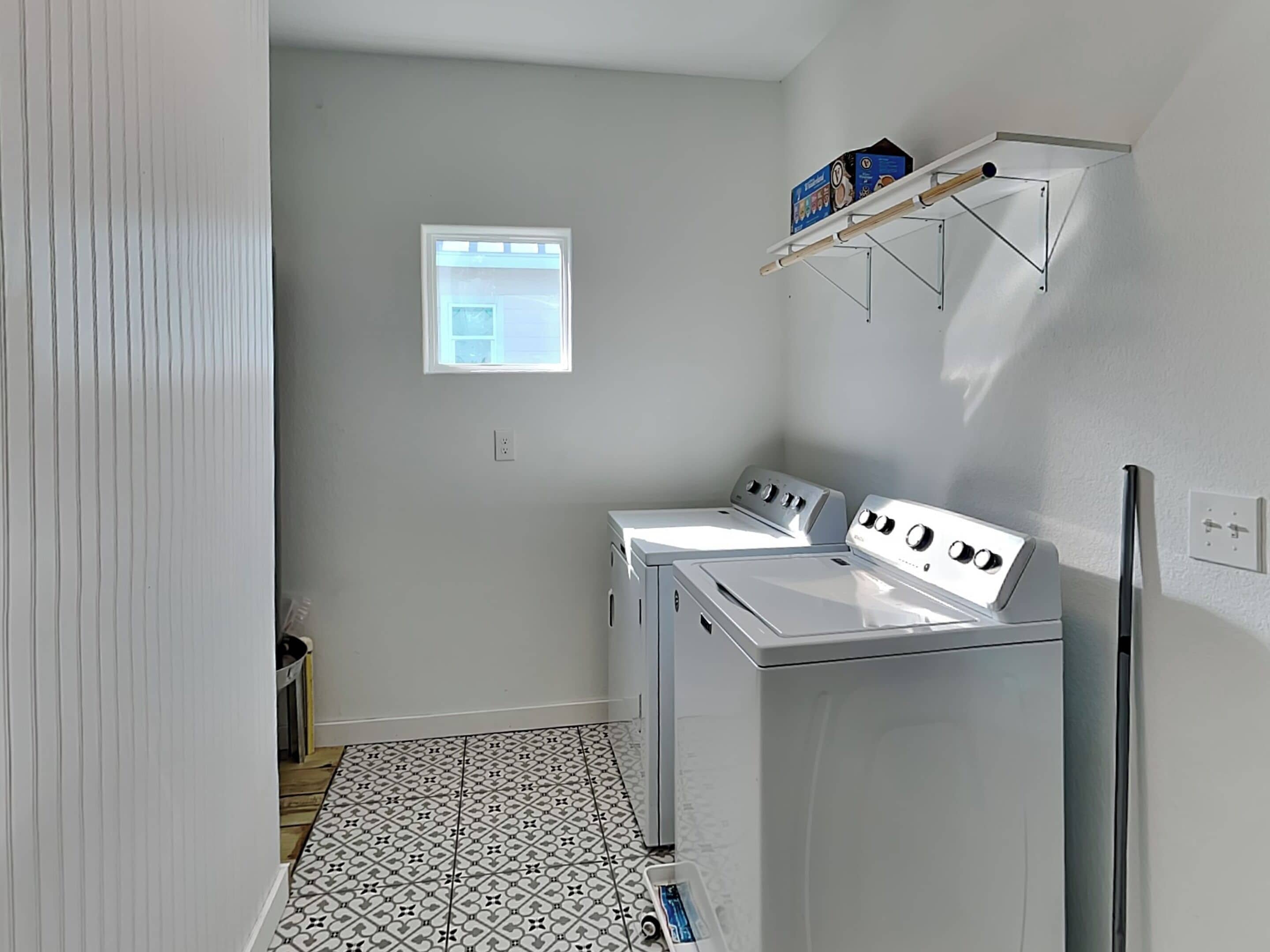 A laundry room with two white washers and dryers, a small window, and a tiled floor.