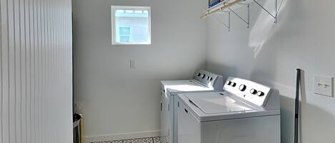 A laundry room with two white washers and dryers, a small window, and a tiled floor.
