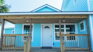 A two-story house with a blue exterior, a white front door, and a wooden porch with railings.