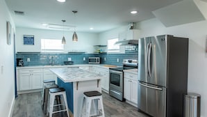 A modern kitchen with a central island, stainless steel appliances, and blue-tiled backsplash.