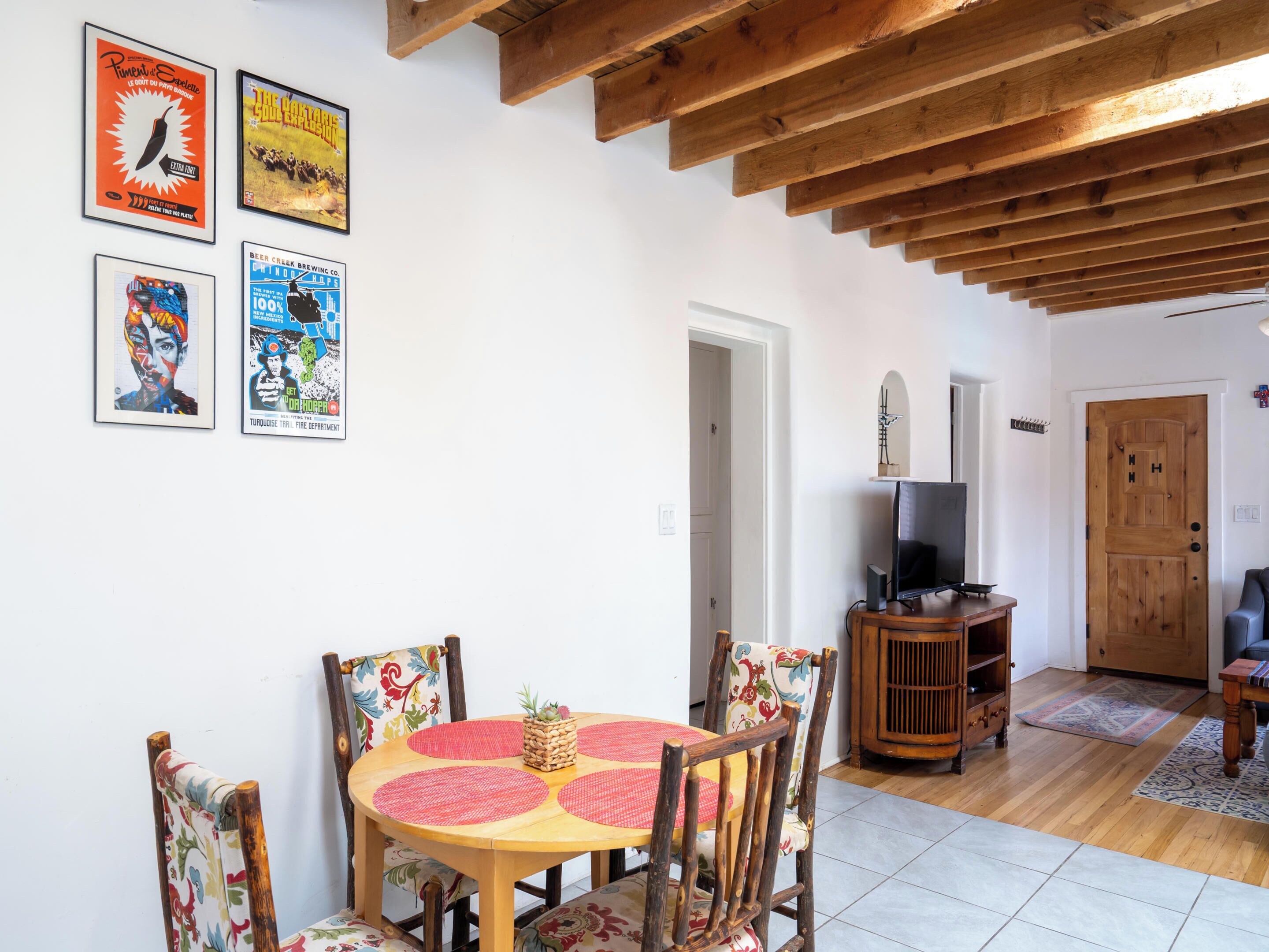 A dining area with a wooden table and chairs, a television on a wooden stand, and a door leading to another room.
