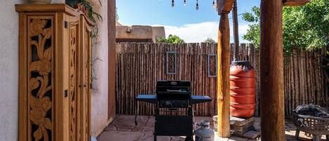 A patio area with a wooden grill, a gas cylinder, and a decorative cabinet.