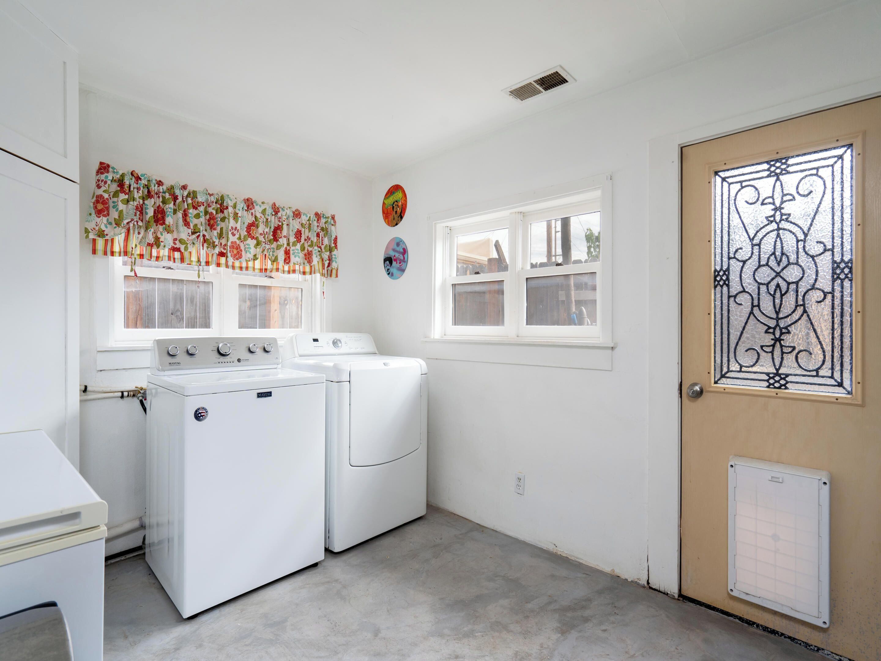 A laundry room with two white washing machines, a window with a view, and a door with a decorative glass panel.