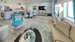 A modern living room with a sofa, a coffee table, and a dining area with a table and chairs. - Mermaids Lair by Silver Sands Vacation Rentals (Port Aransas)