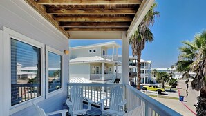 A balcony with white Adirondack chairs, a wooden ceiling, and a view of a beachfront building. - Mermaids Lair by Silver Sands Vacation Rentals (Port Aransas)