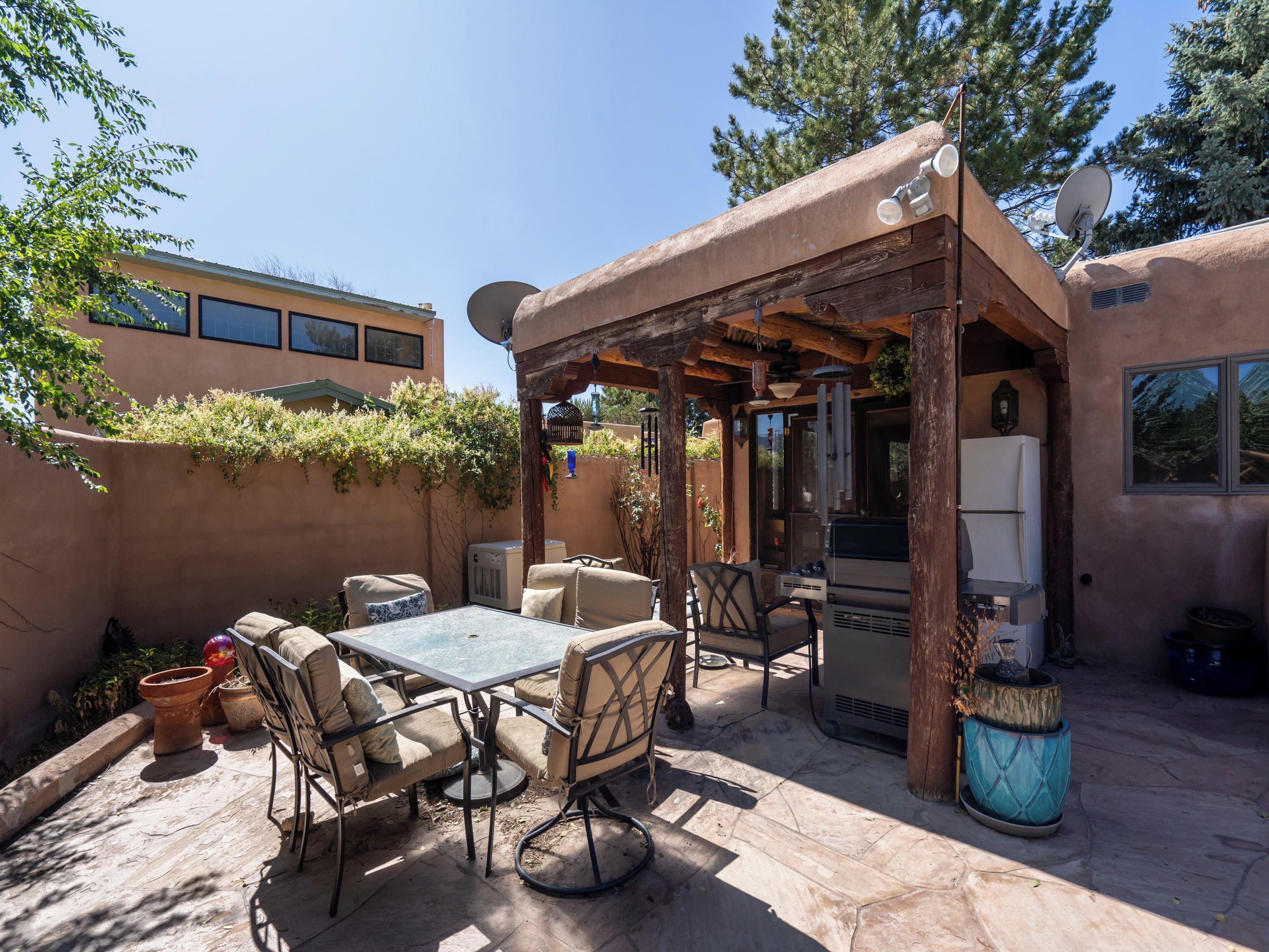 Un patio exterior con mesa y sillas, una parrilla y una pérgola.