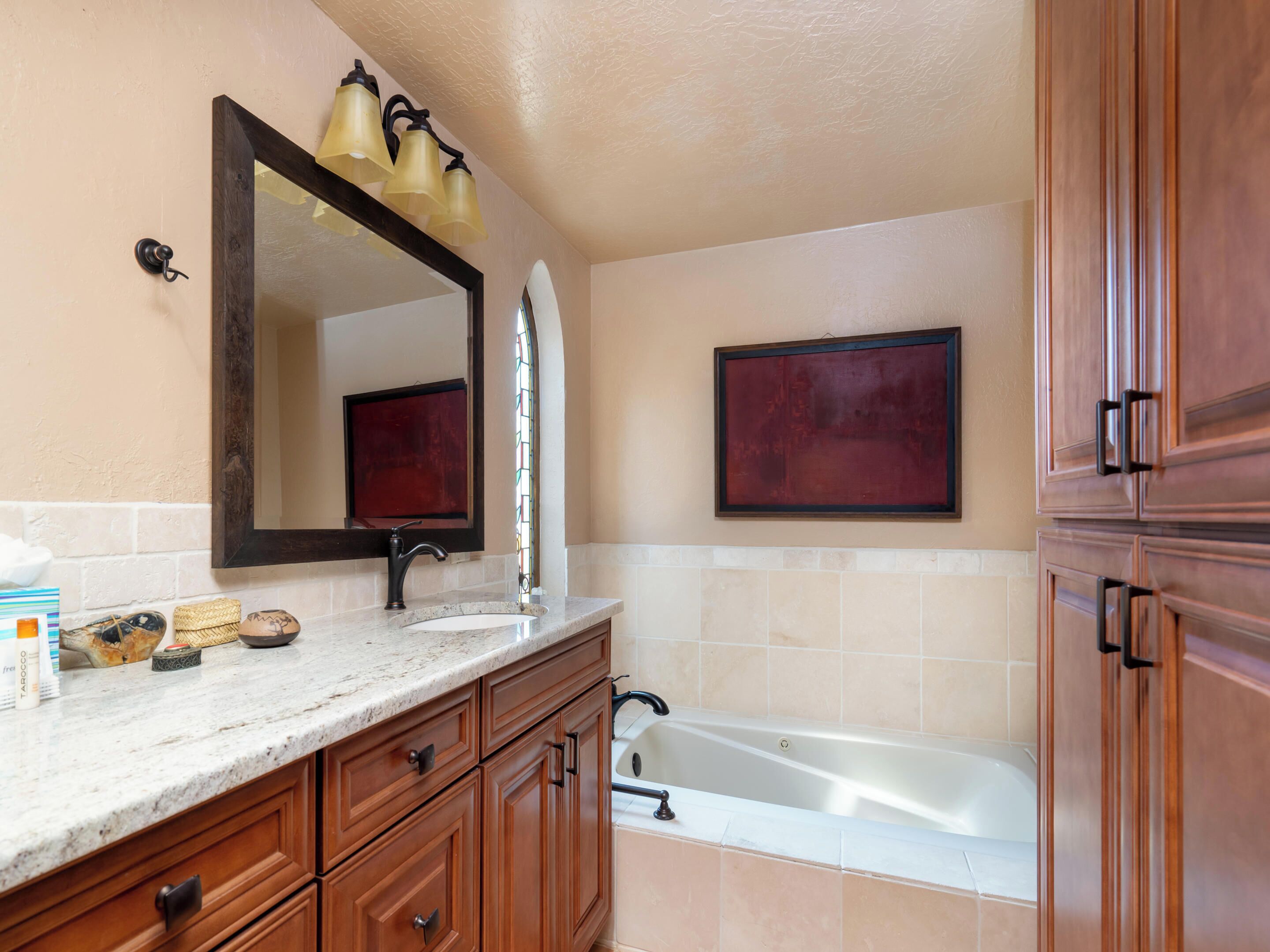 A bathroom with a marble sink, wooden cabinets, a large mirror, a bathtub, and a wall-mounted light fixture.
