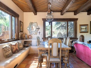 A dining area with a wooden table and chairs, a large mirror on the wall, and a window providing a view of trees. - Rexie's Place by Kokopelli Property Management (Santa Fe)