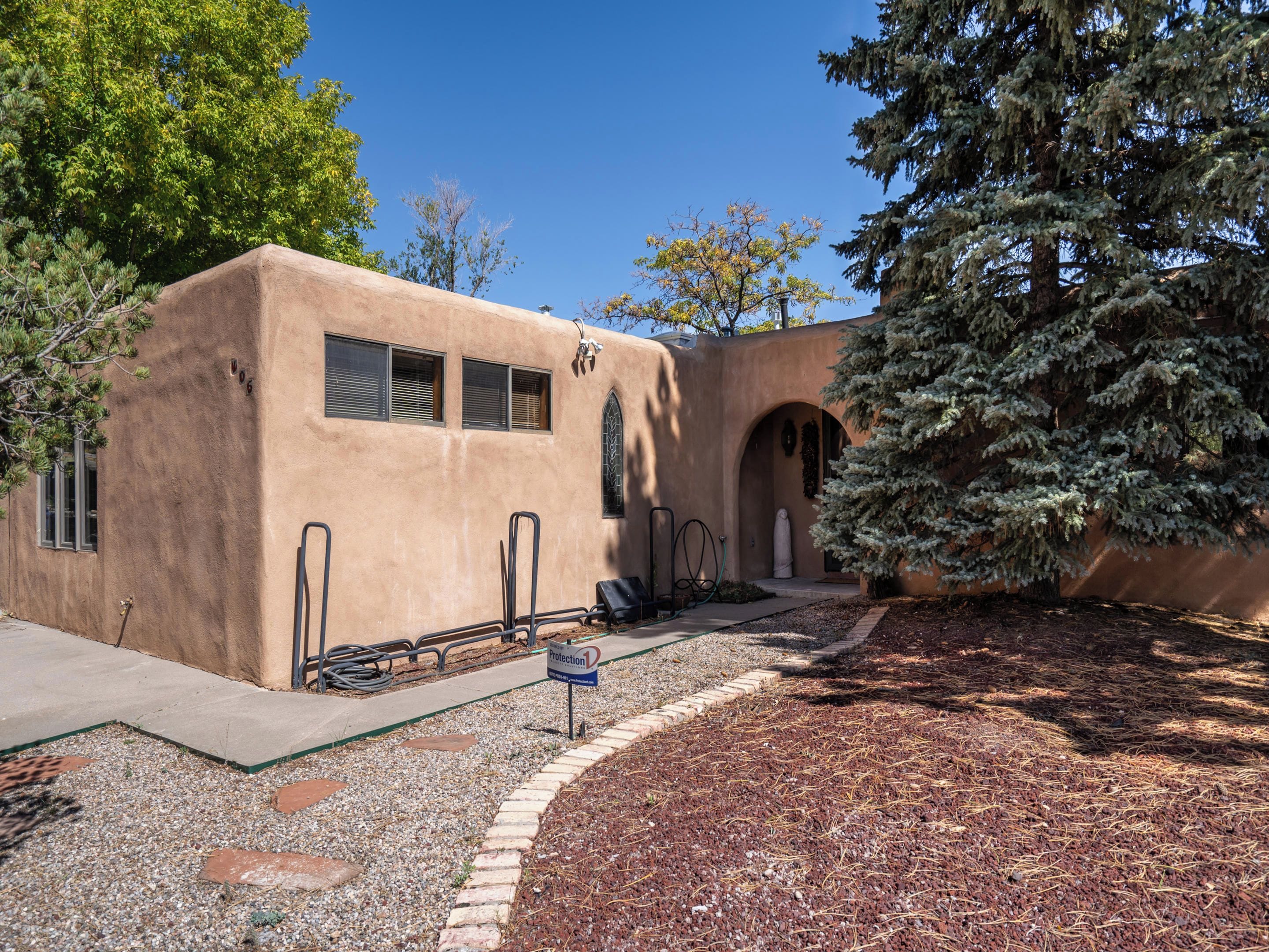 A building with a stucco exterior, a covered patio area, and a large evergreen tree to the right.