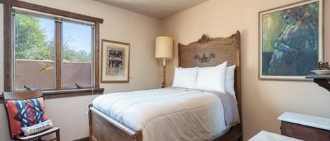 Un dormitorio con cama de madera, una ventana con persianas, una mesita de noche, una silla y un cuadro en la pared.