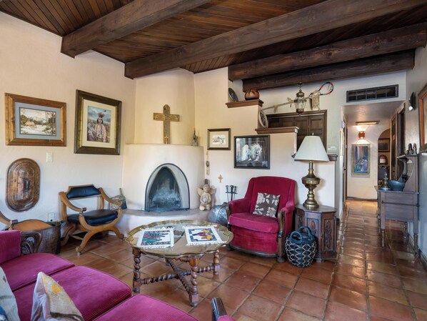Uma sala de estar aconchegante com lareira, vigas de madeira e diversas obras de arte emolduradas.