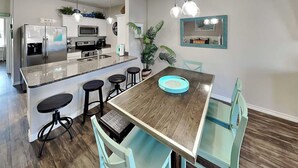 A modern kitchen with a central island, bar stools, a dining table, and a large mirror. - Trestles by Silver Sands Vacation Rentals (Corpus Christi)