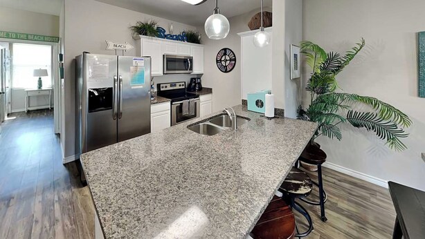 A modern kitchen with granite countertops, stainless steel appliances, and a large island with bar stools. - Trestles by Silver Sands Vacation Rentals (Corpus Christi)