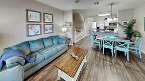 A living room with a blue sofa, wooden coffee table, and a dining area with a table and chairs. - Trestles by Silver Sands Vacation Rentals (Corpus Christi)