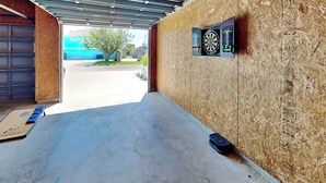 Ett garage med en pilkastartavla upphängd på väggen, en blå matta på golvet och en garageport.