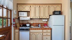 Une cuisine de taille réduite, dotée de meubles de rangement en bois, d’une cuisinière, d’un four à micro-ondes et d’un réfrigérateur.