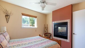 Une chambre à coucher comprenant un lit, un ventilateur de plafond, une fenêtre, un téléviseur fixé au mur et une porte.
