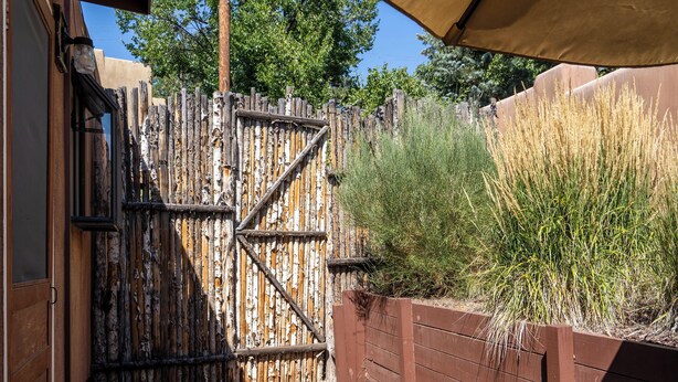 Une porte en bois avec un loquet métallique, un chemin de gravier et une clôture en bois agrémentée de végétation.
