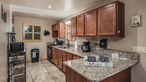 A kitchen with wooden cabinets, granite countertops, a microwave, a coffee maker, and a trash can. - Mountain Flo by Ruidoso Vacation Rentals (Alto)