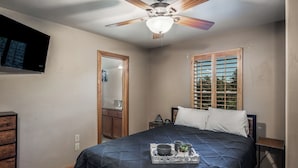 A bedroom with a bed, a ceiling fan, a window with blinds, a dresser, and a TV mounted on the wall. - Mountain Flo by Ruidoso Vacation Rentals (Alto)