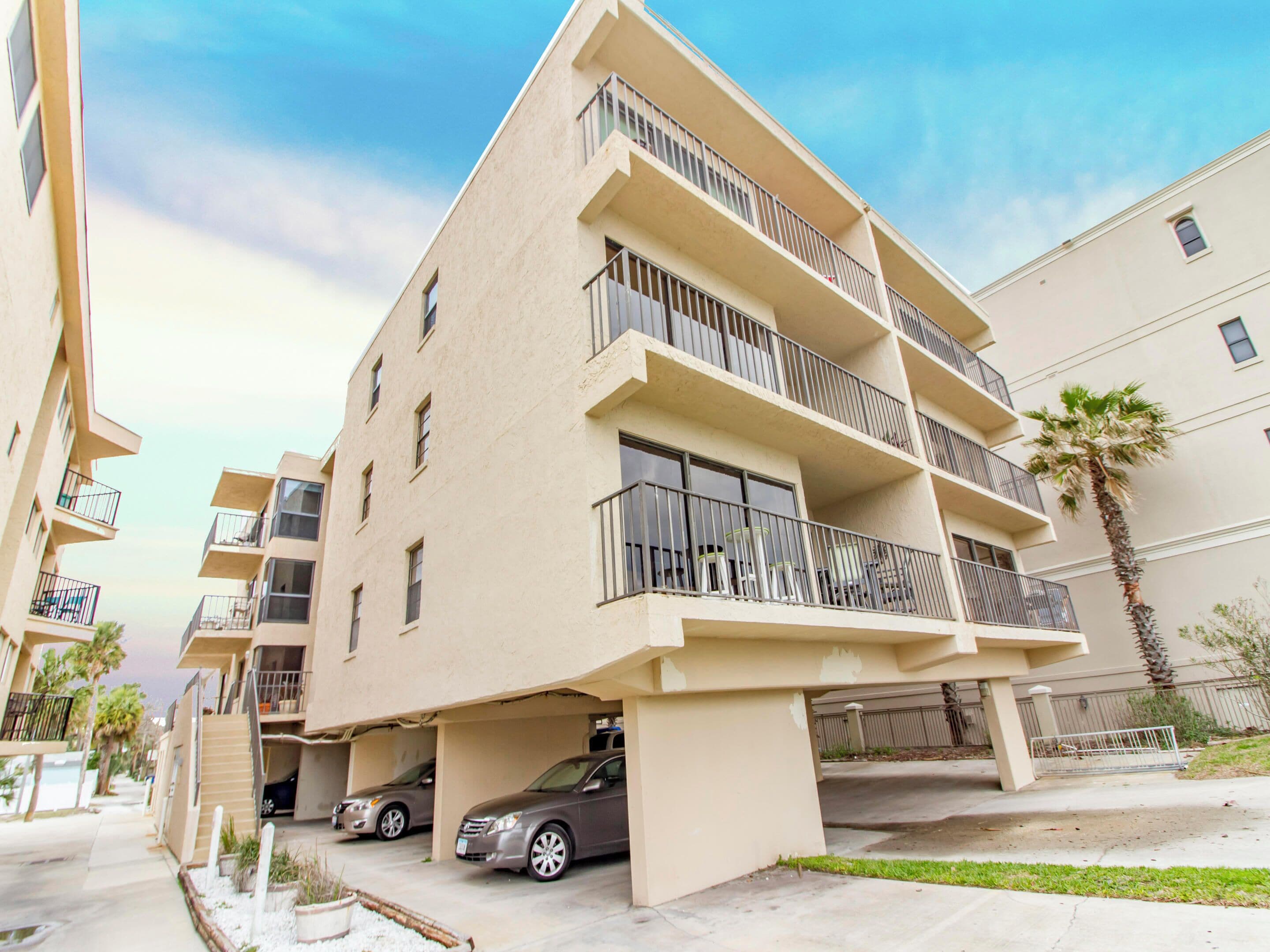 Um edifício residencial com várias andares, varandas, garagem para carros e uma palmeira.