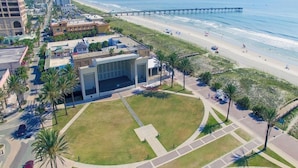 A coastal area with a large open plaza, palm trees, and a beach with a pier. - Beachcomber 403 by Distinctive Beach Rentals (Jacksonville Beach)