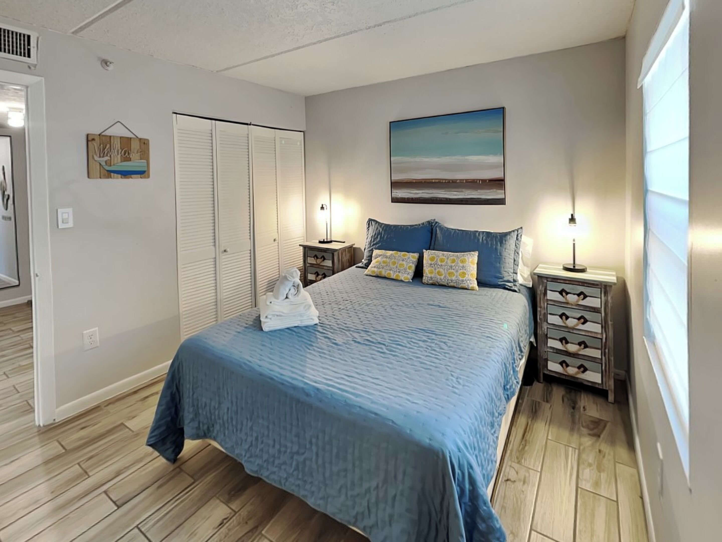 A bedroom with a bed, nightstands, a dresser, a closet, and a painting on the wall.