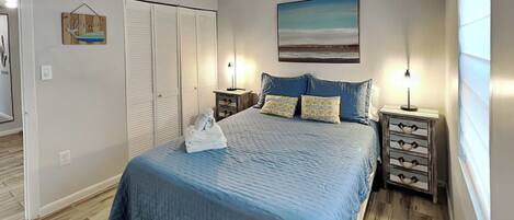 A bedroom with a bed, nightstands, a dresser, a closet, and a painting on the wall.