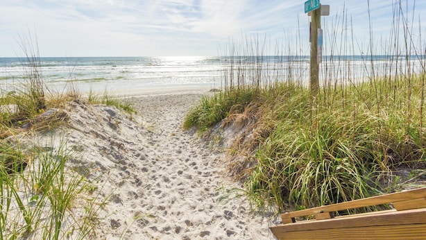 A sandy beach path leading to the ocean with a wooden boardwalk and a street sign. - Beachcomber 403 by Distinctive Beach Rentals (Jacksonville Beach)